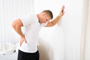 A man leans up against a wall clutching his back in pain.