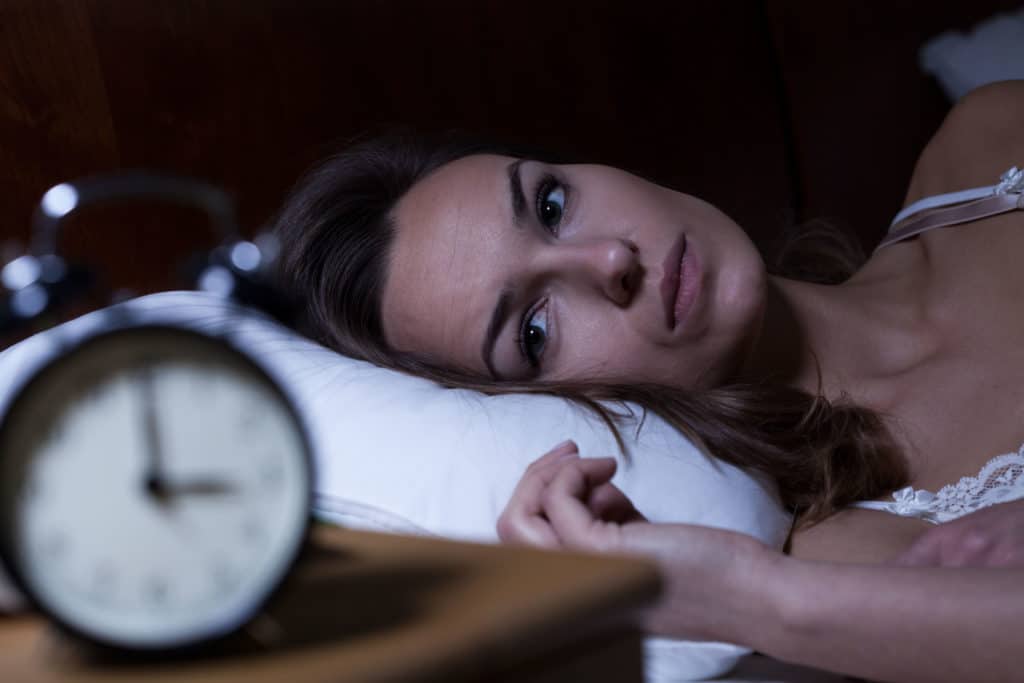 A woman with insomnia is lying in bed and looking at her clock.