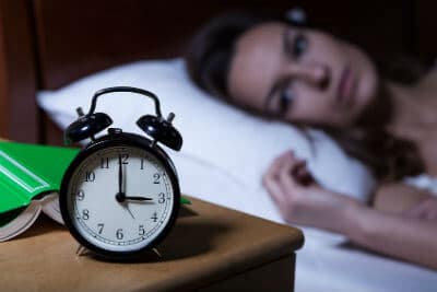 A woman in bed looks over at the bedside clock