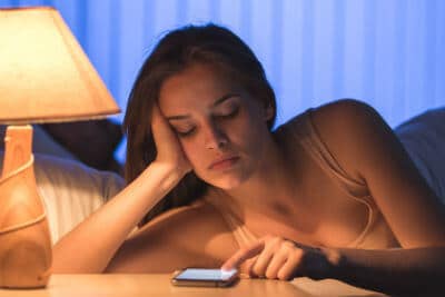 A woman is leaning out of bed to use her phone